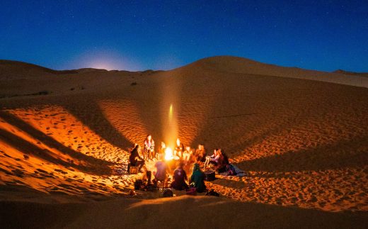 Groupe de personnes autour d'un feu, la nuit, dans le désert