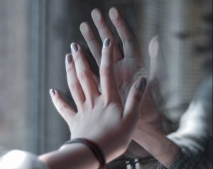 Mains de deux personnes qui se touchent à travers une vitre