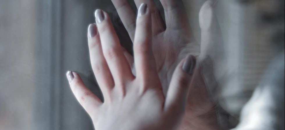 Mains de deux personnes qui se touchent à travers une vitre