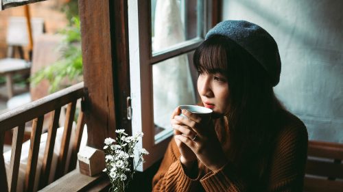 Jeune femme qui boit un café seule en intérieur en regardant par la fenêtre
